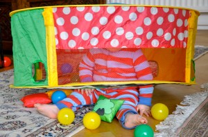 Child with toy on head surrounded by colourful plastic balls. 