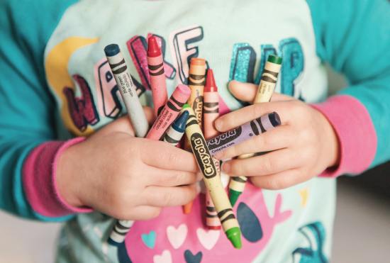 toddler holding assorted coloured crayons